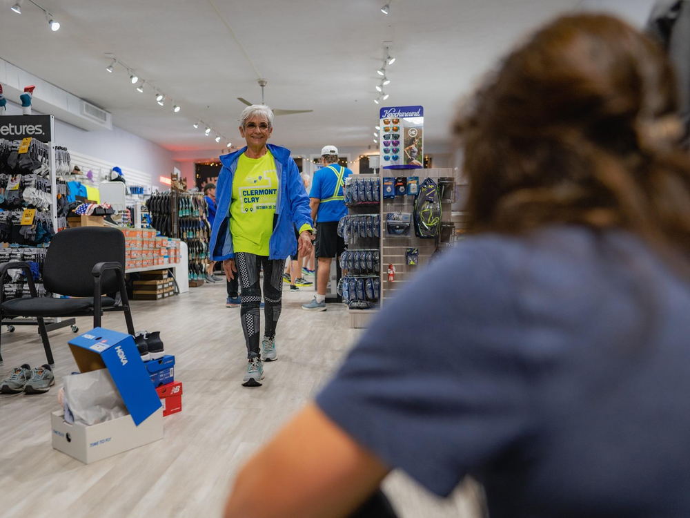 Customer walking toward a Dash Sports fitter for a gait assessment inside the Clermont, FL store, shoe boxes waiting nearby